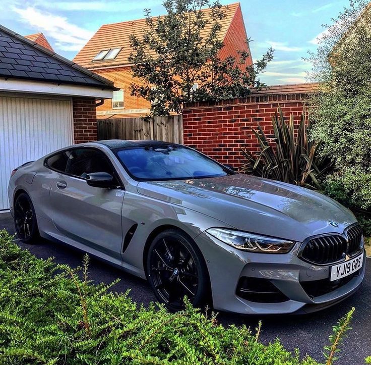 a silver bmw car parked in front of a house next to some bushes and trees