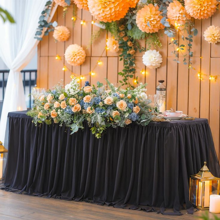 an arrangement of flowers and candles on a table in front of a wall with hanging lights