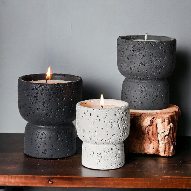 three candles sitting on top of a wooden table next to a tree stump with water droplets