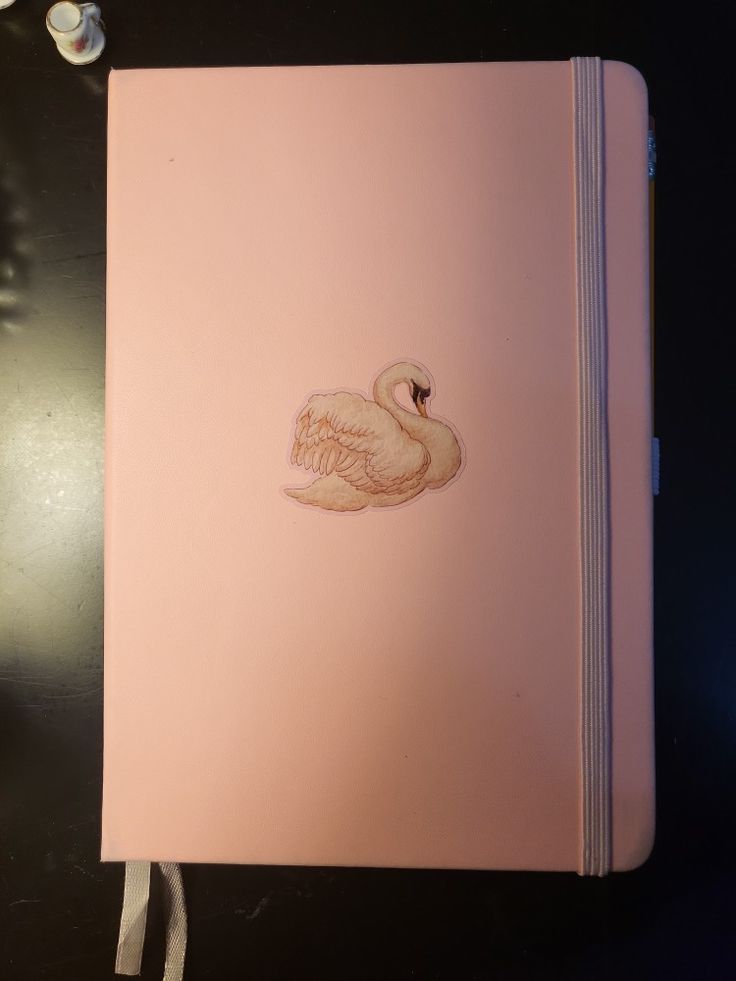 a pink notebook with a white swan sticker on it