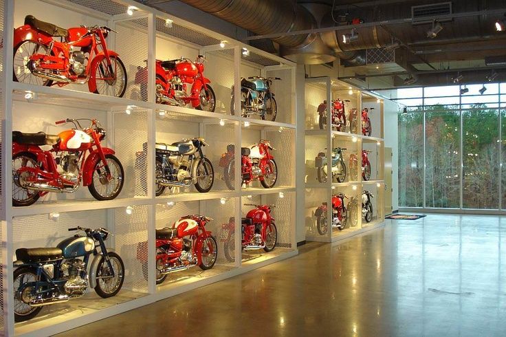 several rows of motorcycles are on display in a room with glass walls and floor to ceiling windows