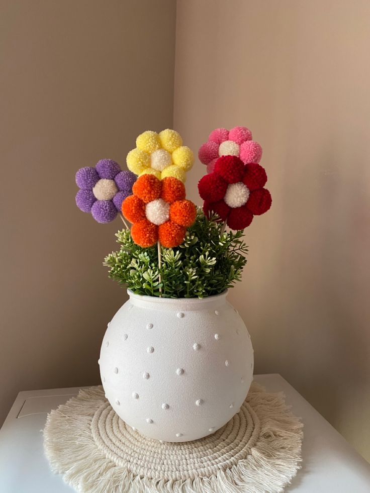 a white vase filled with colorful pom - poms on top of a table