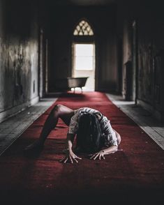 a woman is laying on the floor in an old building with red carpet and light coming through