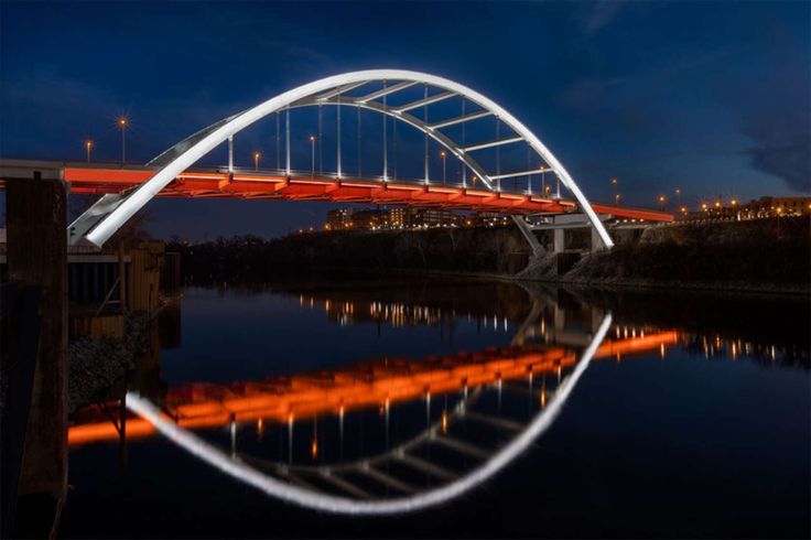 an illuminated bridge over a body of water at night with lights reflecting in the water