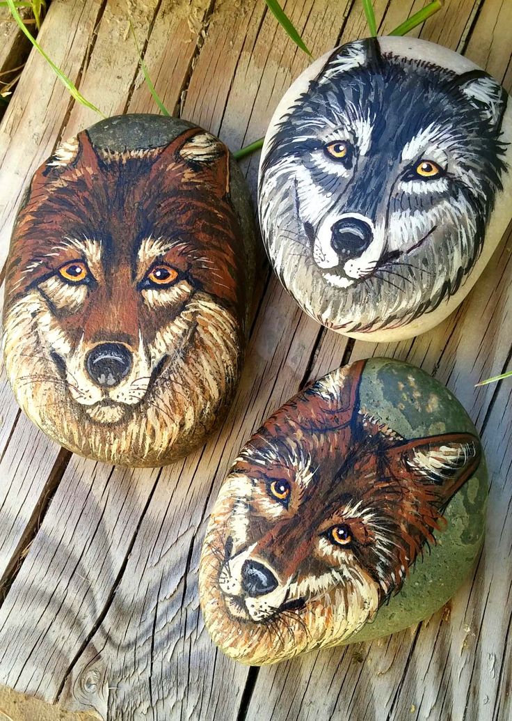 three painted rocks sitting on top of a wooden floor next to green grass and leaves