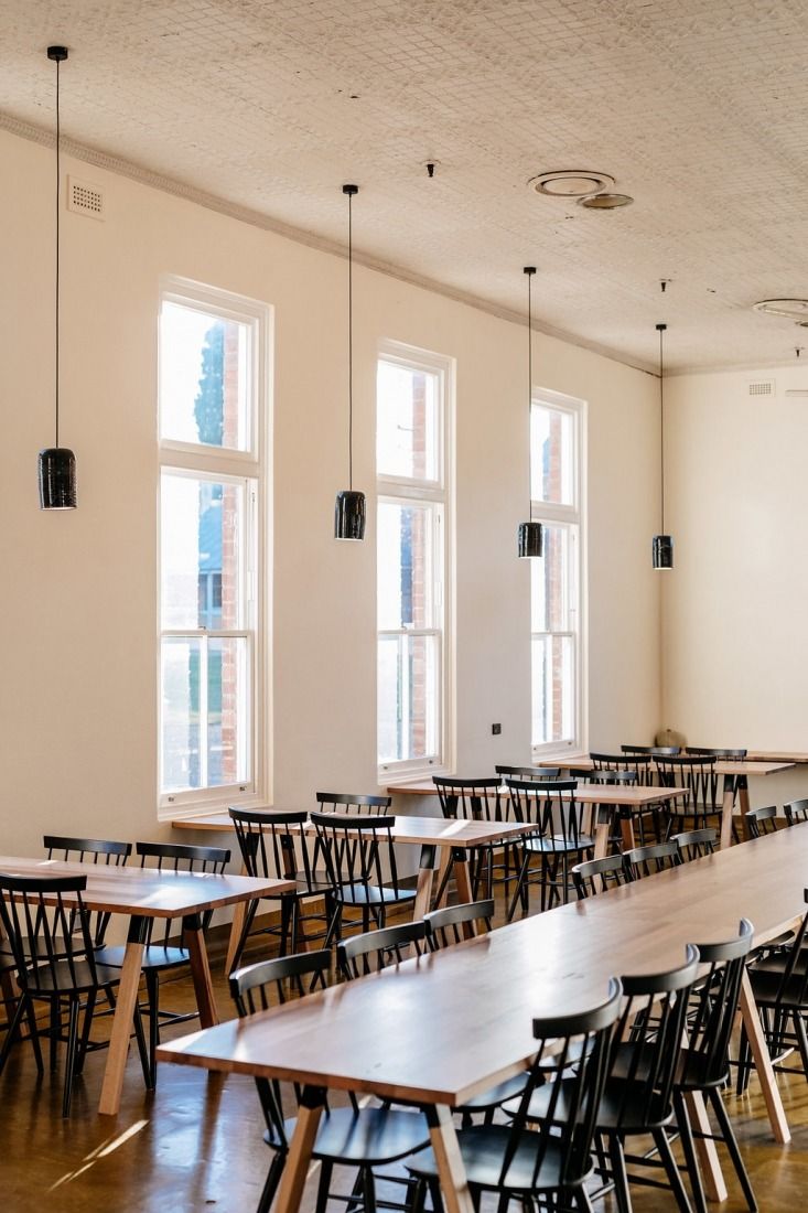 an empty classroom with tables and chairs in front of two large windows on the wall