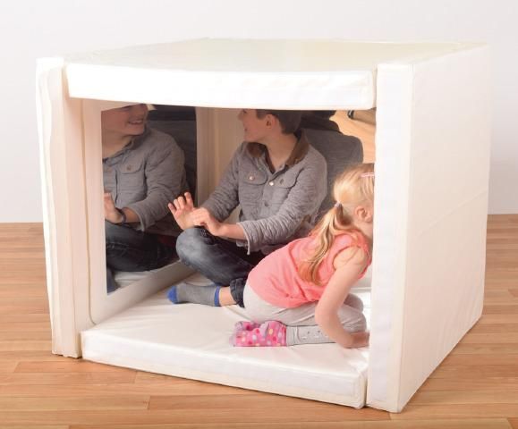 two adults and a child sitting in a small white box on the floor with wood floors