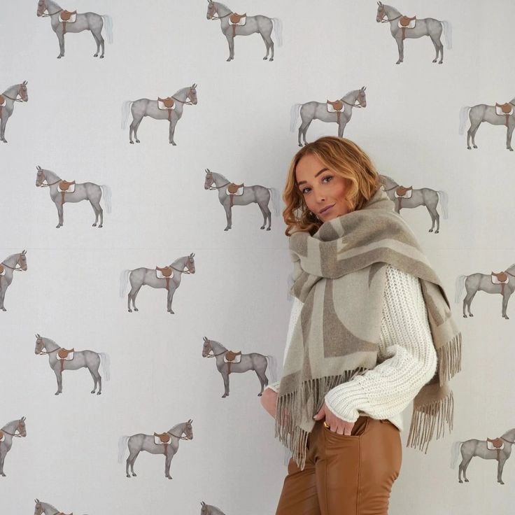 a woman standing in front of a wall with horses on it's back and scarf around her neck