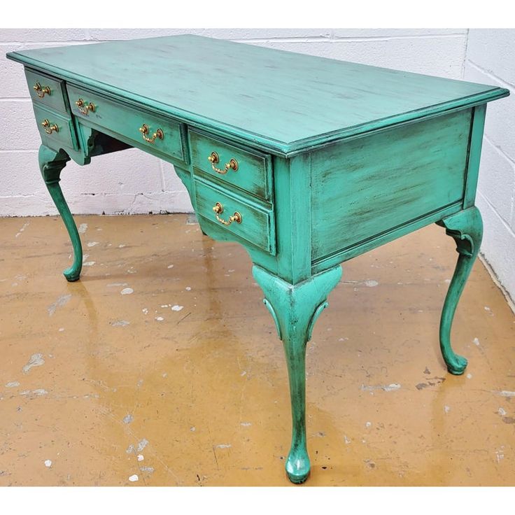 a green desk with two drawers sitting on top of a floor next to a brick wall