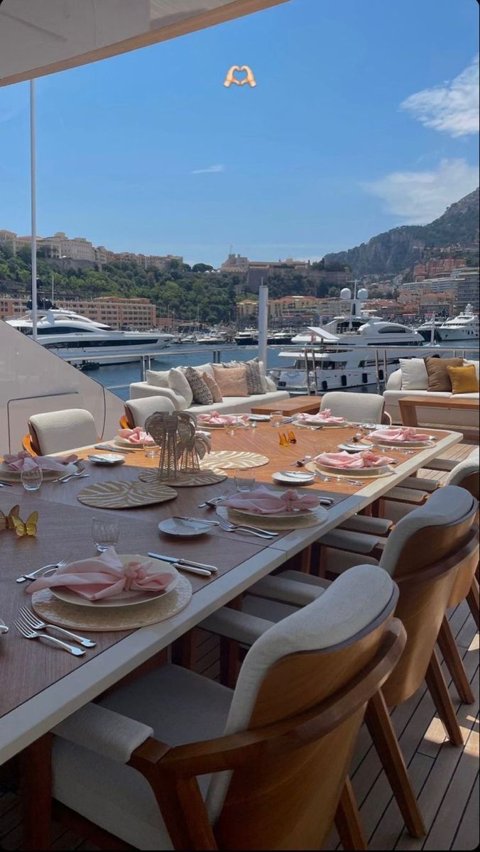 an outdoor dining area with tables and chairs on the deck overlooking boats in the water