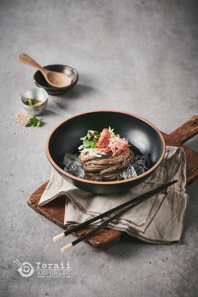 a bowl with noodles and vegetables in it on a wooden tray next to chopsticks