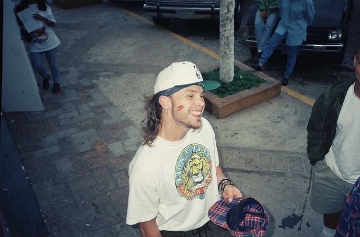 a man in a white shirt and hat walking down the street with other people behind him