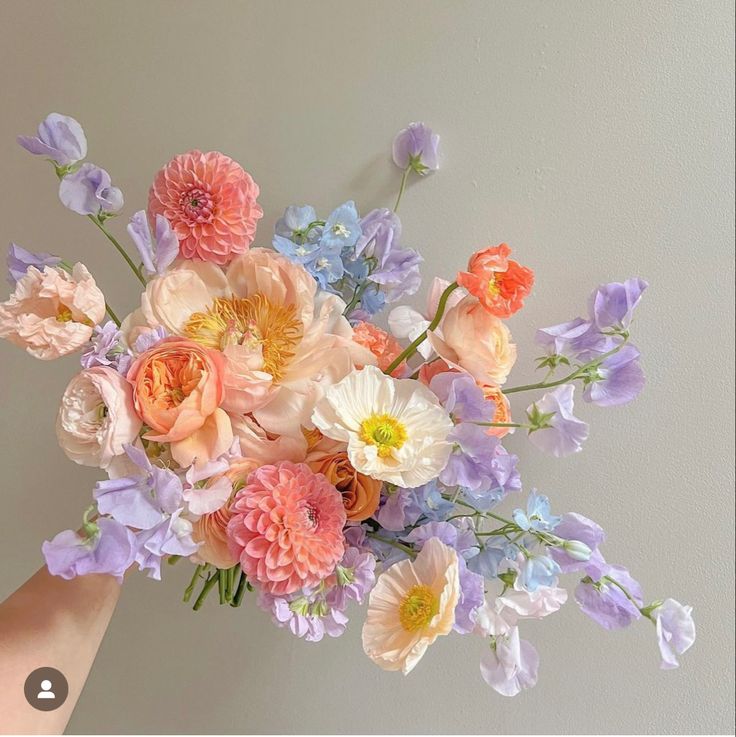 a bouquet of flowers is being held up by someone's hand in front of a wall