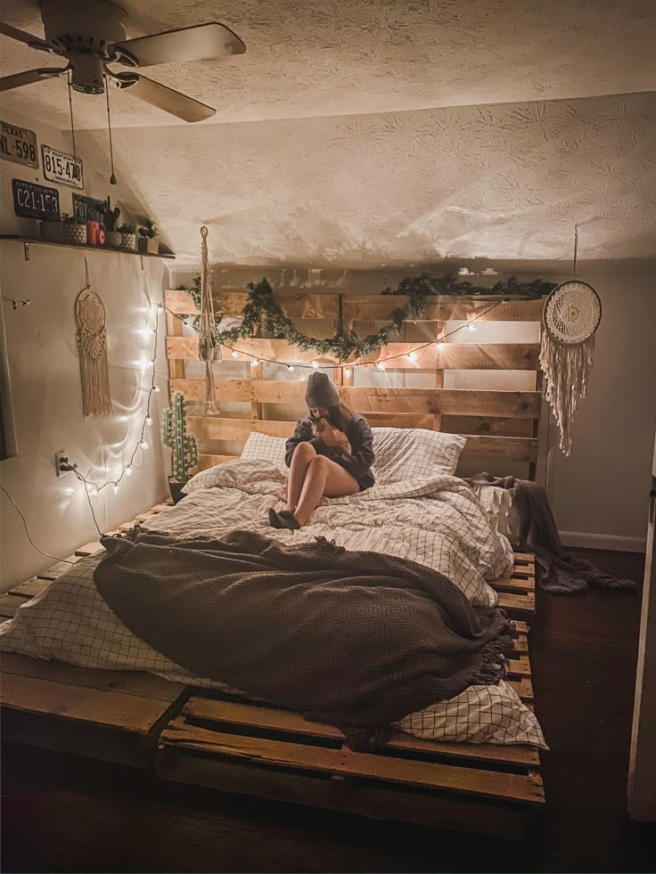 a woman sitting on top of a bed in a room with wooden pallets and lights