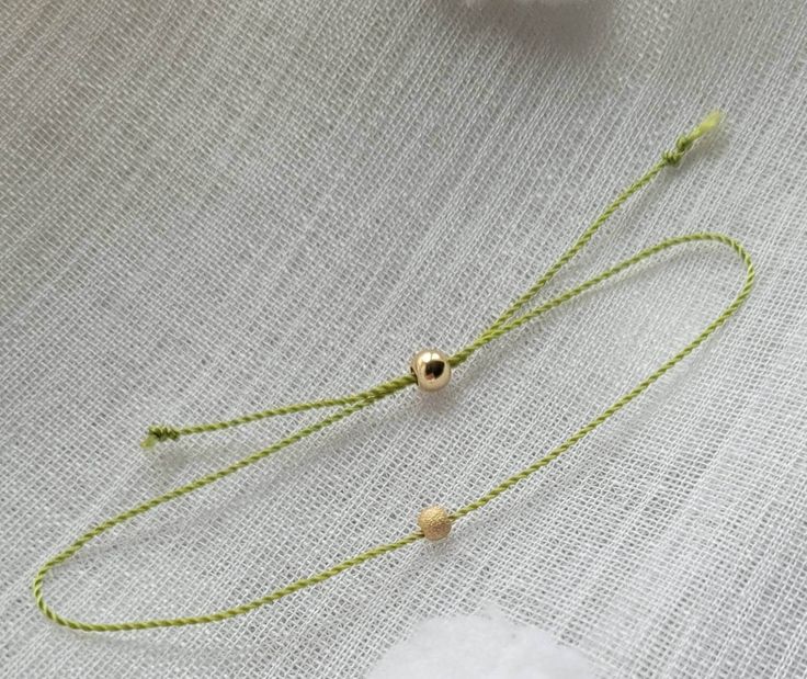 a close up of a necklace on a white cloth with flowers in the back ground