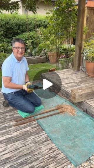 a man sitting on a wooden deck pouring wine into a bottle with two bamboo sticks in front of him