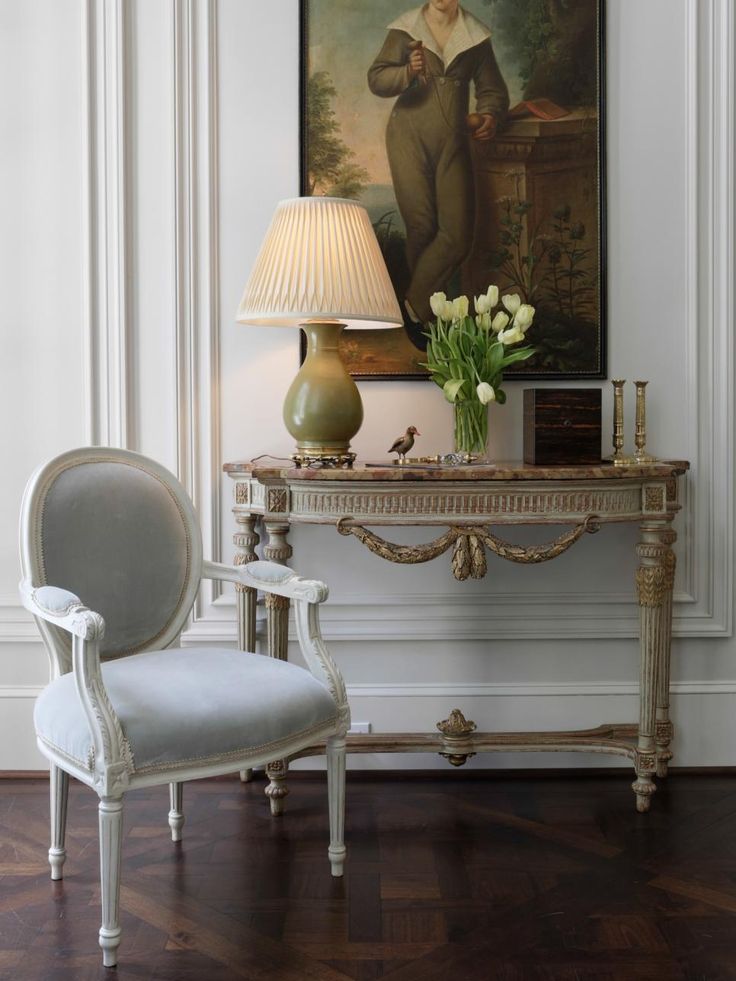 a white chair sitting next to a table with a lamp and painting on the wall