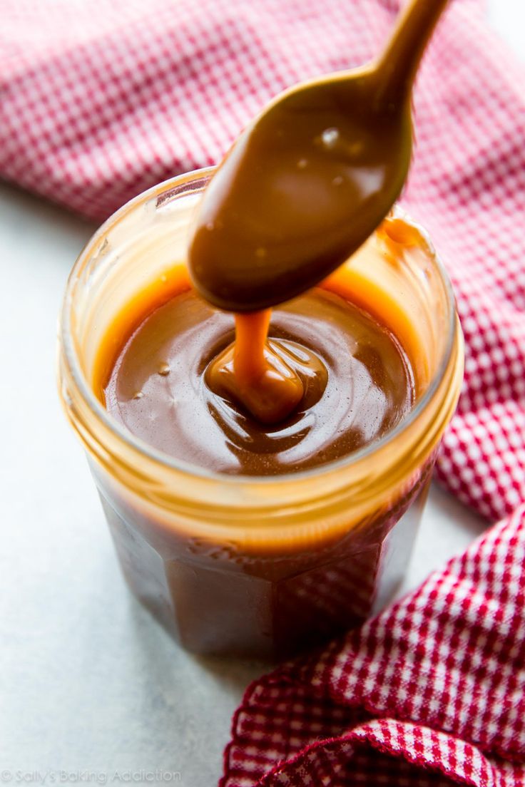 a spoon full of caramel sauce on top of a jar with a red and white checkered cloth