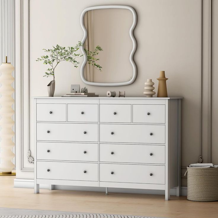 a white dresser sitting next to a mirror and vase with a green plant on top