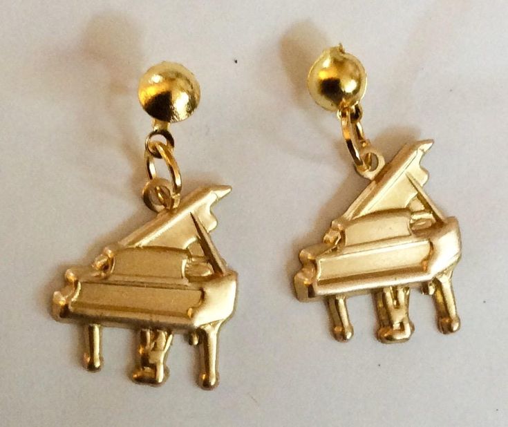 two gold tone musical instruments are hanging from earwires on a white surface, one is shaped like a piano and the other is shaped like a piano