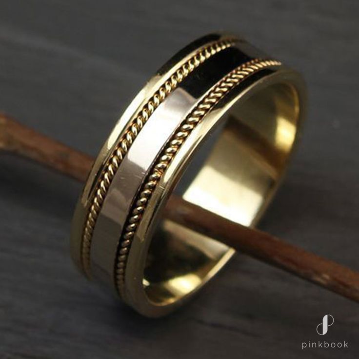 a gold wedding ring with braiding on the side and a wooden stick next to it