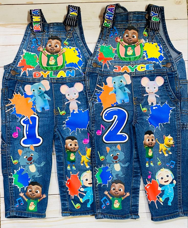 two children's denim overalls with cartoon characters and numbers on them, one is blue