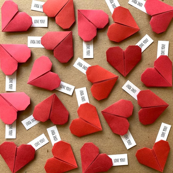 red paper hearts with name tags attached to them sitting on a brown surface next to each other