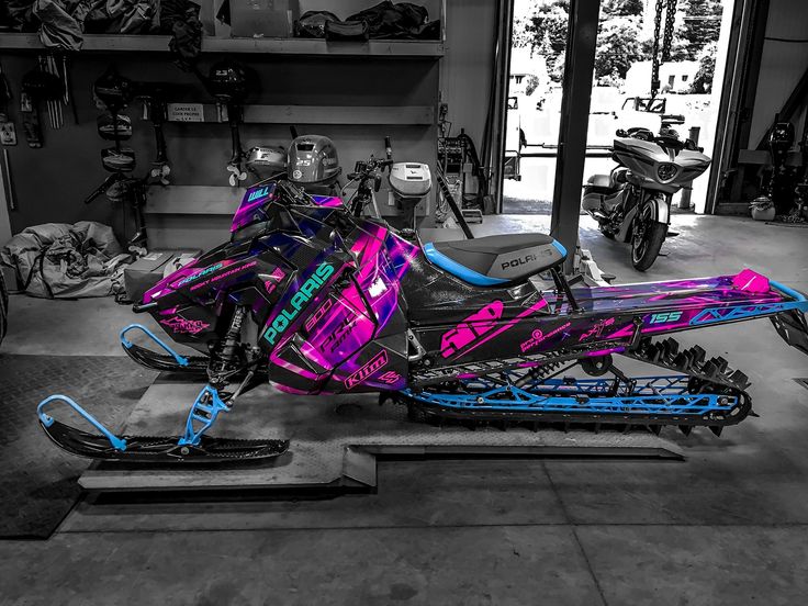 a pink and blue snowmobile parked in a garage next to a motorcycle on the ground