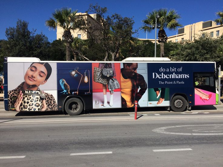 a bus that has advertisements on the side of it's side in front of palm trees