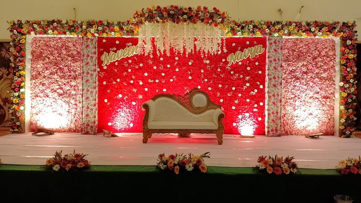 a stage set up for a wedding ceremony with red and white flowers on the wall