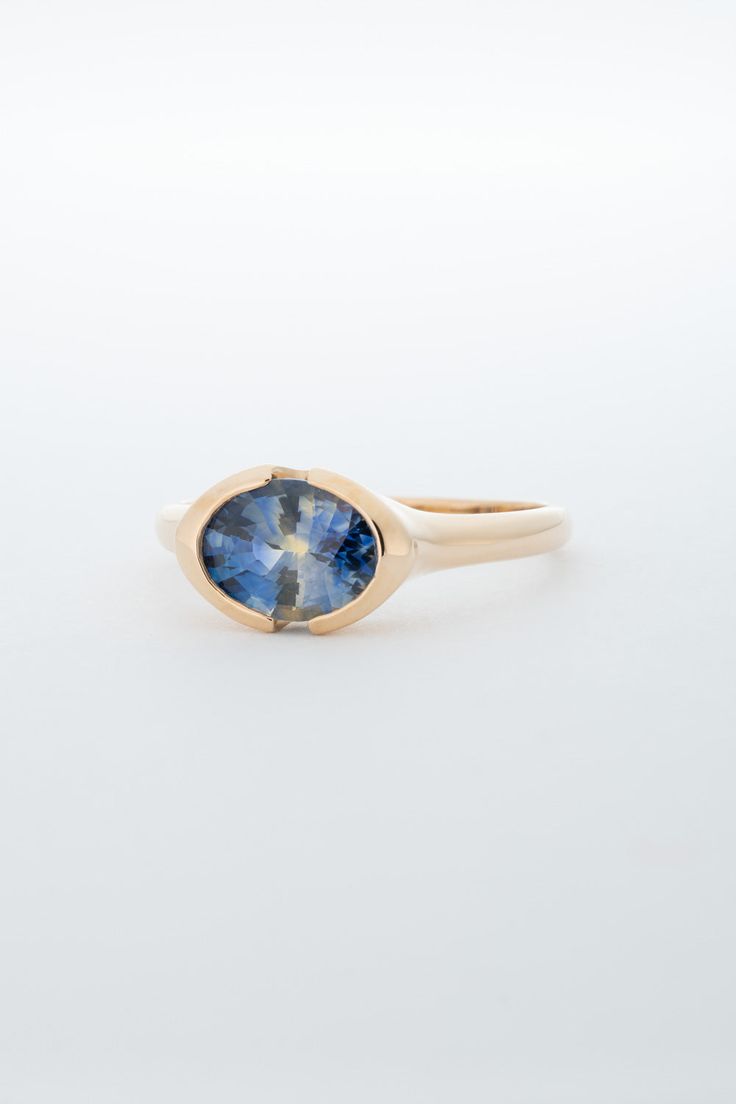 One of a kind solitaire ring, featuring a Blue Yellow White Parti Sapphire Oval. The Sapphire is parti color, meaning the stone shows two or more distinct colors within the single stone. This Sapphire features blue, yellow, and white colors and is set in a 18k Yellow Gold split bezel setting in East-West orientation. One of a Kind Piece. Stone: Oval Cut Parti Sapphire / Heated / 1.67 cts / Ethically sourced. Metal: 18k Yellow Gold Size: Ring is currently a Size 7 but can be adjusted to order. East West Sapphire Engagement Ring, Oval Sapphire Ring, Parti Sapphire, Sapphire Solitaire, Dream Engagement, Dream Engagement Rings, Pretty Jewelry, Single Stone, White Colors