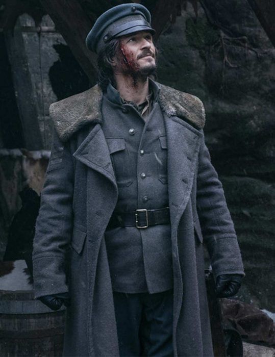 a man in grey coat and black hat standing next to a barrel with blood on it