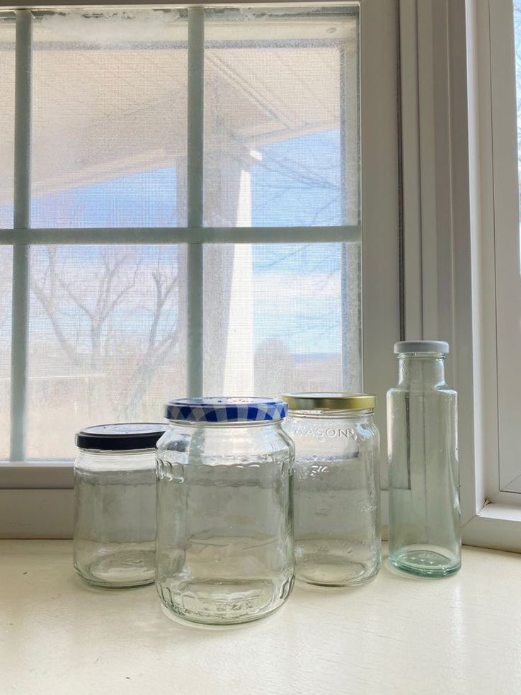 three glass jars sitting on top of a counter next to a window