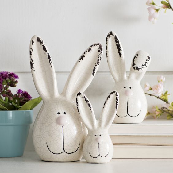 two white ceramic rabbits sitting next to each other on a table with flowers in the background