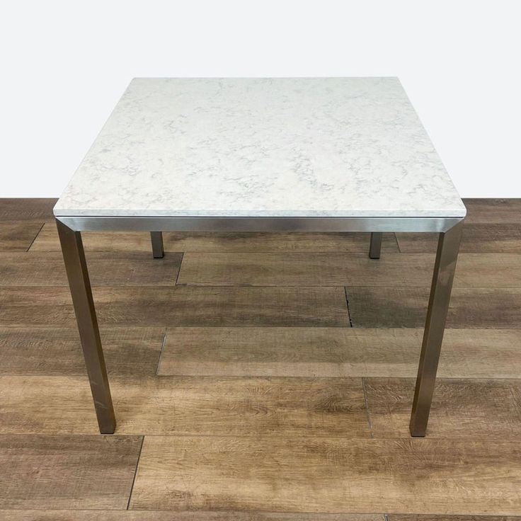 a white marble top dining table with metal legs on a wood flooring area in front of a white wall