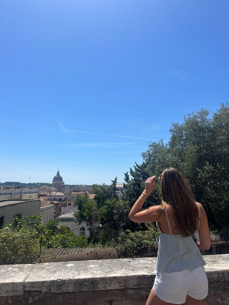 a woman standing on top of a stone wall looking at the sky and buildings in the background