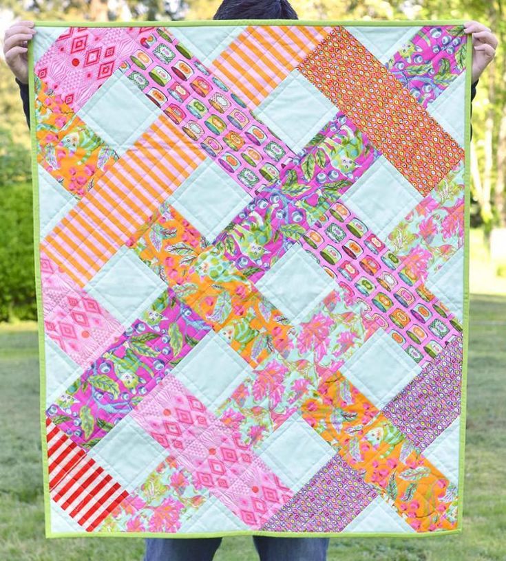 a person holding up a colorful quilt in the grass