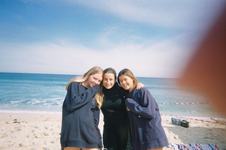 three girls are standing on the beach together