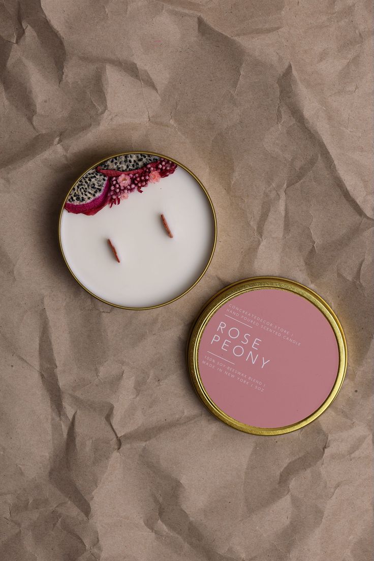 a candle in a tin next to a pink and white box with the words rose peony on it