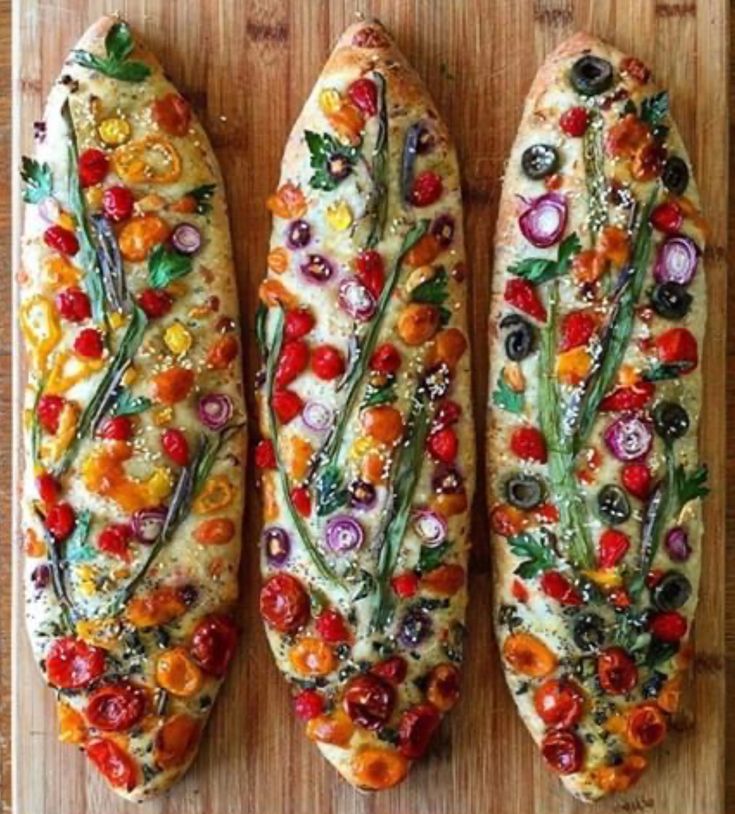 three different types of bread on a cutting board with tomatoes, onions, and other veggies