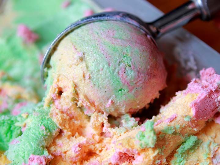 a scoop of colorful ice cream sitting in a bowl next to a metal scooper