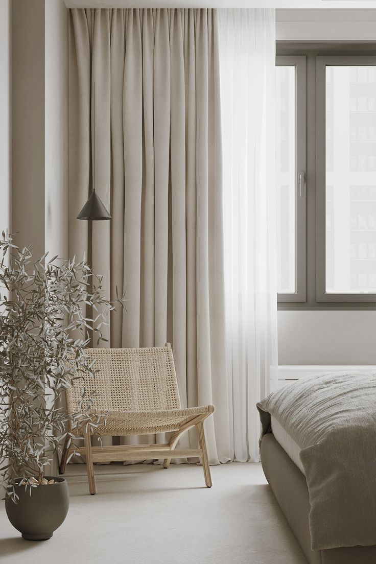 a bed sitting next to a window in a room with white curtains and a wicker chair