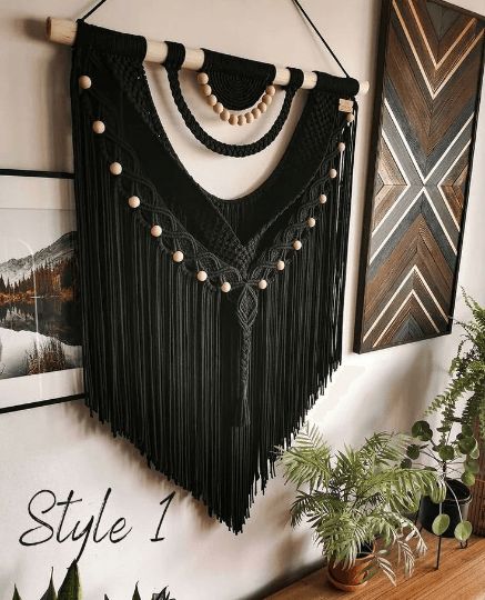 a wall hanging with beads and tassels on it next to a potted plant