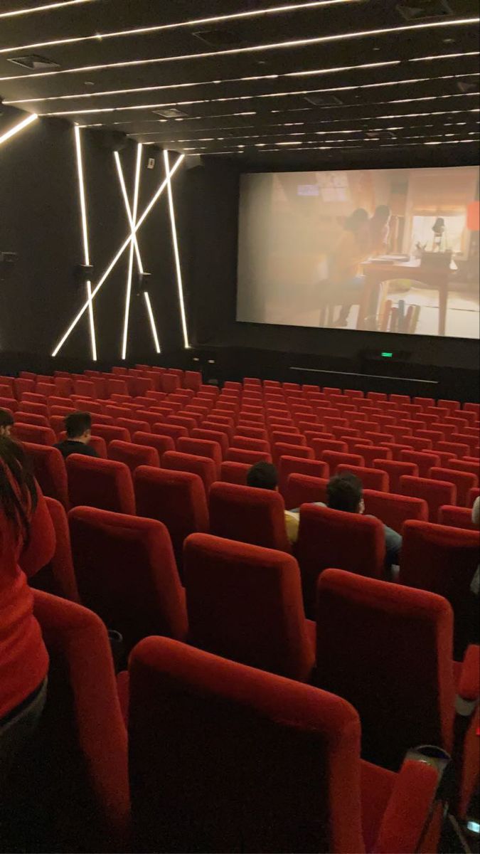 people sitting in red chairs watching a movie on the screen at an auditorium or theater