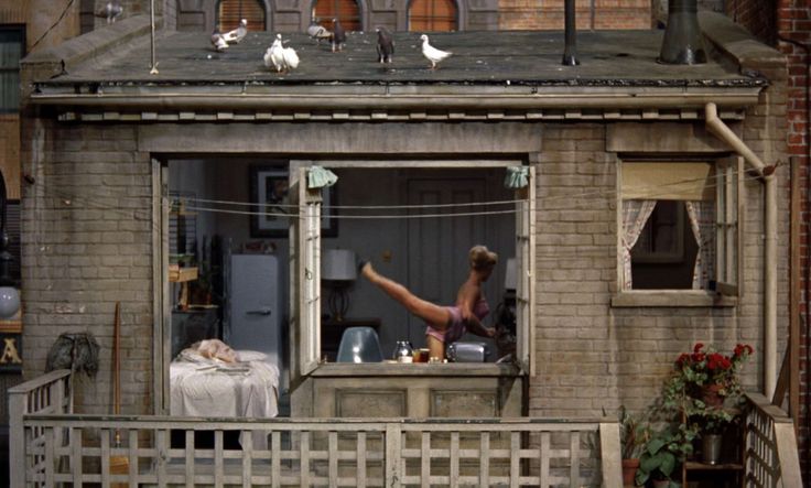 a woman is standing in the window of a house with birds on top of it