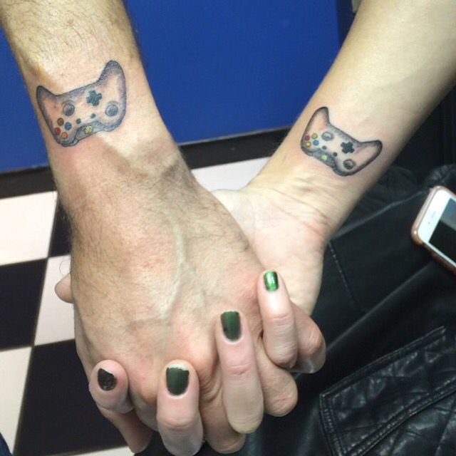 two people holding hands with matching tattoos on their arms and one has a cat head