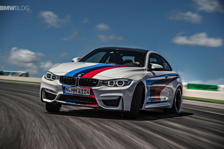 a white and blue car driving down a race track with clouds in the background on a sunny day