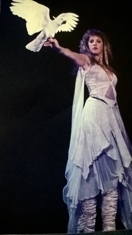 a woman holding a white bird in her right hand while standing on a black background