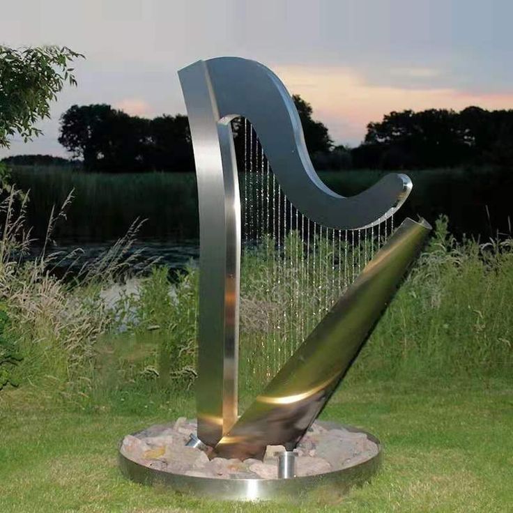 a large metal harp sitting on top of a lush green field