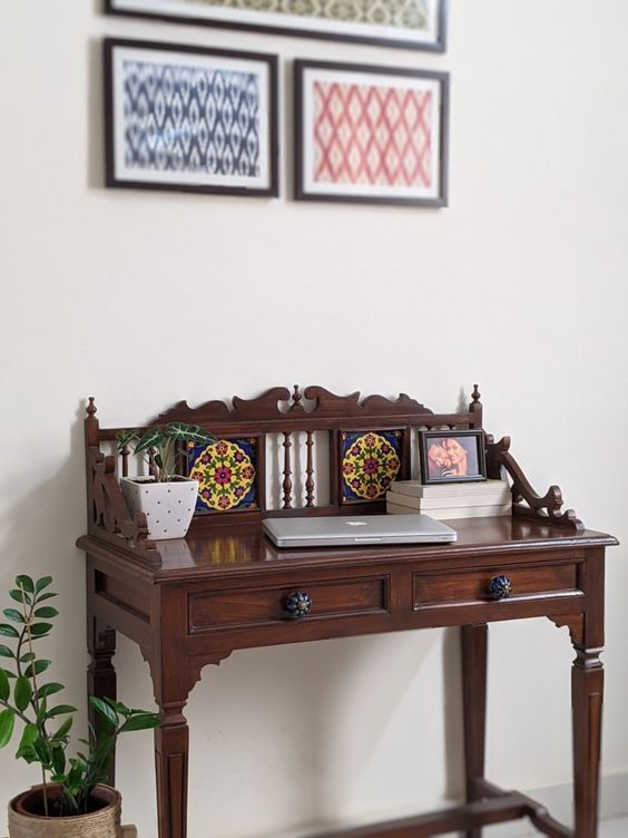 a wooden desk with pictures on the wall above it and a potted plant next to it